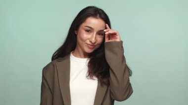 Kendine güvenen, neşeli bir jestle genç bir kadının portresi. Saçlarını deniz mavisi bir arka plana atıyor. Cazibe ve pozitiflik saçıyor..