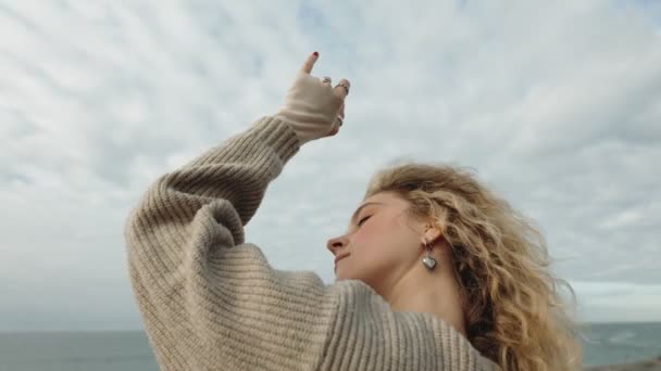 風を感じる若い女性の芸術的なイメージは 海辺のセーターで優雅に動き 自由と表現を体現しています — ストック動画