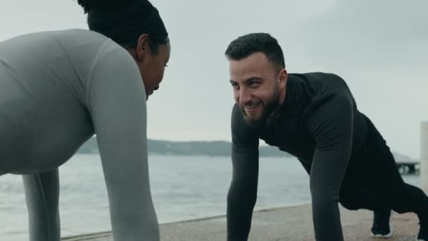 ウォーターフロントのトレーニングのために準備する運動服の2人の人 モチベーションとアクティブなライフスタイルに焦点を当てて コア筋をトレーニング — ストック動画