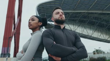 Çeşitli fitness ikilisi, açık şehir arka planına karşı idman ekibi gibi davranırken, ortaklığı ve gücü sembolize ediyor..