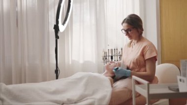 Doğal ışıklandırılmış bir kuaförde odaklanmış bir güzellik uzmanı sakin bir kaplıca ortamında uzman cilt bakımı sağlayan sakin bir müşteriye yüz bakımı yapar..
