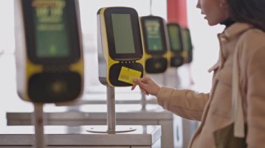 A young adult woman taps a card on a contactless reader at a transit gate at train station