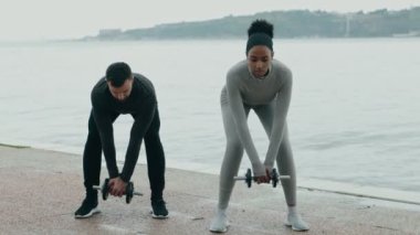 Atletizmde çeşitli bir çift, nehir kenarındaki sırt kasları, takım çalışması, sağlık ve açık hava sporları ile ağırlık kaldırıyor..