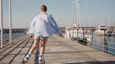 Genç bir kadın marinada güneşli bir günün tadını çıkarırken paten kayıyor ve dans ediyor. Neşeli ve kaygısız açık hava aktivitesi.