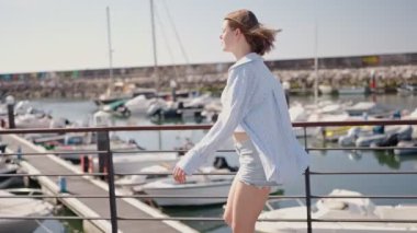 Genç bir kadın güneşli bir günde yat limanında paten kayıyor, açık hava ve boş zamanların tadını çıkarıyor..