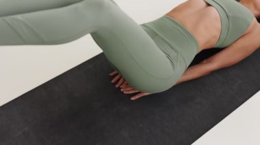 Atletizm kıyafetleri içinde tanınmayan bir kadın karın kaslarına odaklanmış, vücut esnekliği ve kontrolü gösteren bir yoga asanasının göstergesidir..