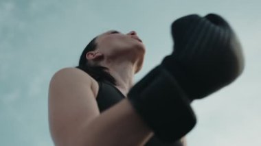 Eldivenli kararlı bir kadın boksör bulutlu bir gökyüzünün altında ısınır, gücünü gösterir ve odaklanır..