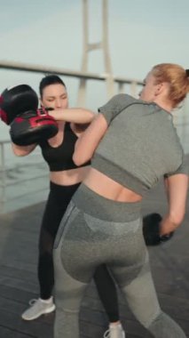 İki atletik kadın dışarıda boks antrenmanı yapıyorlar. Güç, zindelik ve kararlılık gösteriyorlar..