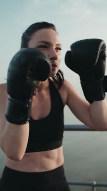 30 'larında kararlı bir kadın, aktif giysi giyiyor, dışarıda boks eldivenleriyle antrenman yapıyor. Gücünü ve sağlığını arttırmak için..