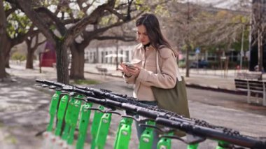 Genç bir kadın akıllı telefonuyla şehir ortamında elektrikli scooter kiralamak için bir QR kodunu tarıyor..