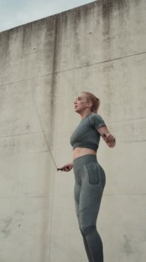 Genç atletik kadın dışarıda spor yapıyor. Enerjik bir şekilde beton bir arka planda ip atlıyor..