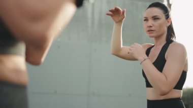 Kişisel antrenörle boks tekniklerini uygulamaya odaklanmış bir müşteri, azim ve güç duygusu ile dışarıda..