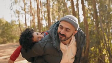 Yürek ısıtan bir an, mutlu oğlunu sırtında taşıyan gülümseyen bir babayı huzur dolu bir ormanda yakalar..