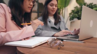 İki çalışkan öğrenci ödevlerini ahşap bir masada dizüstü bilgisayar ve not defteriyle yapıyorlar..