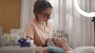 Yetenekli bir kozmetikçi, sakin bir güzellik salonundaki yüz bakımı sırasında sakin bir bayan müşterinin yüzünü nazikçe siliyor..