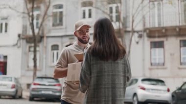 Neşeli bir kurye, şehir ortamında bir kadın müşteriye bir paket teslim ediyor ve günlük hizmet anı yakalıyor..