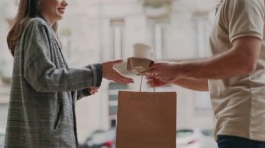 Tanımlanamayan kurye, evinde gülümseyen bir kadına kağıt torba ve kahve fincanı veriyor..