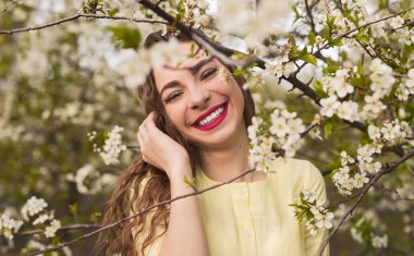 Sarı gülücükler takan neşeli bir kadın bahçesinde çiçek açan bahar çiçekleriyle çevrili, mutluluk ve sükunet saçan.