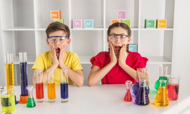 Güvenlik gözlüğü takan iki sürpriz çocuk laboratuarda renkli kimya deneyleri yapıyor, heyecan ve keşif sergiliyorlar..