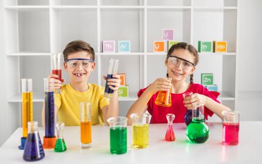 Koruyucu gözlük takan gülümseyen çocuklar, sınıfta renkli bir kimya deneyi yapıyorlar. Bizzat öğrenme, merak ve eğitimi teşvik etme.