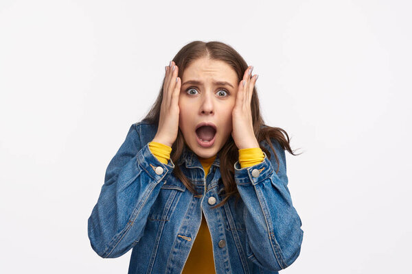 Portrait of young woman in denim jacket with a shocked and surprised expression on white background.