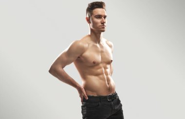 Kaslı bir adam stüdyo ortamında kendine güvenerek poz veriyor. Formda ve atletik bir fiziği var. Fitness, sağlık ve yaşam tarzı kavramları için ideal görüntü.