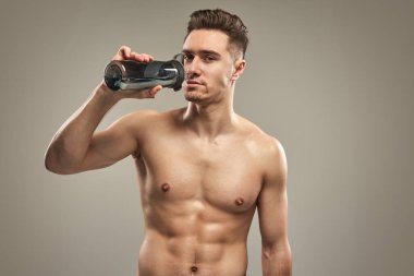 Formda bir adam idmandan sonra şişeden su içiyor. Sağlıklı yaşam tarzı, fitness, hidrasyon ve egzersiz konsepti.