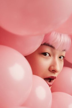 Pembe balonlarla çevrili güzel bir kadının yakın plan portresi neşeli ve tuhaf bir atmosfer yaratıyor..