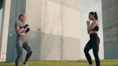 Isınma egzersizleri yapan iki atletik kadın açık hava ortamında boks antrenmanına hazırlanıyor..