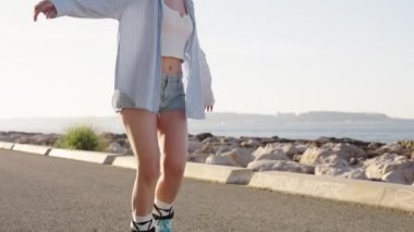 Çekici genç bir kadın gün doğumunda asfalt bir rıhtımda paten kayıyor, özgürlük ve kaygısız neşe duygusunu somutlaştırıyor..