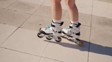 Güneşli bir günde dışarıda paten kayan birinin yakın çekimi. Kiremit kaplı bir yüzeyde beyaz patenler içinde ayaklar.