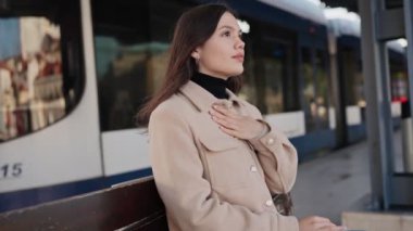 Düşüncelere dalmış genç bir kadın istasyondaki bankta tek başına oturmuş, trenini bekliyor..