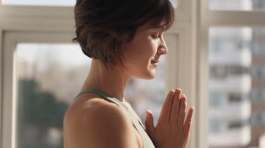 Güneşli bir odada meditasyon yapan, sükunet ve farkındalığı somutlaştıran huzurlu bir kadının yan görüntüsü..