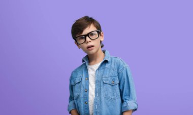 Young boy with glasses and a denim jacket looking shocked and surprised against a purple background. Expressive and engaging image. clipart