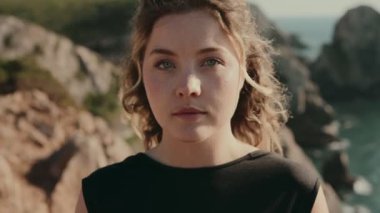 Doğal bir geçmişi olan bir kadının yakın plan portresi, kayalık bir manzaranın ortasında, düşünceli ve huzurlu bir ifadeyi gösteriyor..