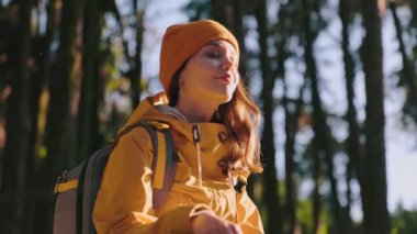 Huzurlu, gözleri kapalı, sakin bir orman yürüyüşü sırasında güneşlenen, sükuneti ve doğayla olan bağlantısını somutlaştıran genç bir kadın..