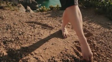 Çıplak ayaklı kadın kumlu zeminde zarif bir şekilde dans ediyor, ayaklarıyla daireler çizerek modern bir dans ediyor..