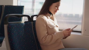 Genç bir kadın, akıllı telefonuyla meşgul olurken, doğal ışık altında huzurlu bir tramvay yolculuğunun tadını çıkarıyor..