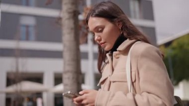 Genç bir kadın akıllı telefonuyla şehrin sokaklarında yürüyor. Muhtemelen yolunu bulmak için navigasyon uygulaması kullanıyor..