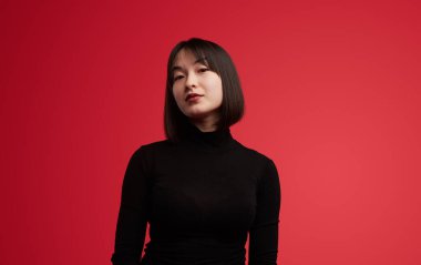 Siyah balıkçı yaka giyen, kendine güvenen bir kadının portresi, canlı kırmızı bir arka plana karşı poz veriyor. Moda, tutum ve cesur ifade.