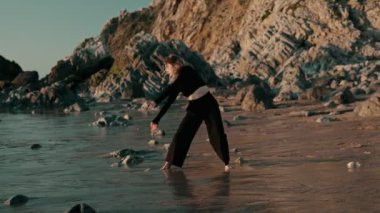 Sahilde sanatsal bir poz veren zarif bir dansçı. Huzurlu bir ortamda doğal güzelliği ve hareket özgürlüğünü kucaklıyor..