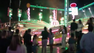 Bulanık, rüya gibi görüntüler. İnsanlar lunaparkın ve lunaparkın atmosferinin tadını çıkarıyorlar..