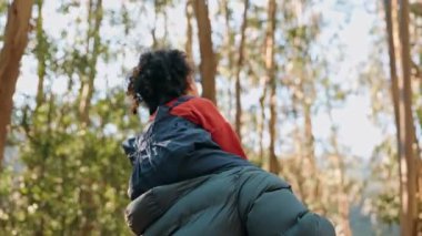 Yürümeye başlayan bir çocuk, orman macerası sırasında yetişkin bir omuzuna tünemiş, kaygısız bir neşe ve aile bağını özetleyen bir zevk ifade eder..