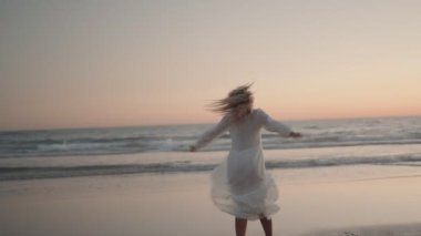 Beyaz elbiseli kaygısız bir kadın güzel bir sahilde dans ediyor. Güneş okyanusun üzerinde batarken dalgalar çarpıyor. Mutluluk, özgürlük ve mutluluk hissi..
