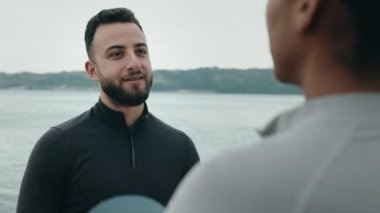 Bir fitness koçu, deniz kenarındaki bir antrenmandan sonra siyah bir bayan sporcuyla dostça bir konuşma yapar..