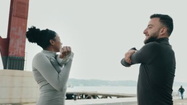 Kişisel antrenör ve siyah bir kadın kollarını deniz kenarında uzatarak antrenmana hazırlanıyorlar..