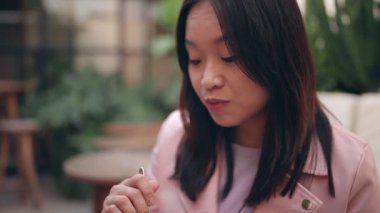 Asyalı bir kadının mutlu bir şekilde tatlı yediği, elinde kaşık tuttuğu, çerçevesi dışında biriyle sohbet ettiği yakın plan..