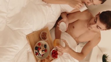 Yatakta kahvaltı yapan bir çiftin genel bakış açısına göre, meyve ve granola ile sağlıklı bir şekilde yayılmış, sıcaklık ve samimiyet yayıyor..