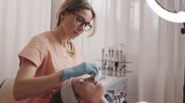 Yetenekli bir kozmetikçi, bir kadının yüzünü nazikçe silerek modern bir kuaförde cilt gençleştirme tedavisine hazırlıyor..