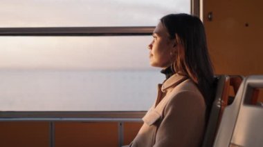 Düşünceli genç bir kadın feribot penceresinden dışarı bakar. Yolculuğu boyunca güneşin sıcacık parıltısıyla ıslanır..